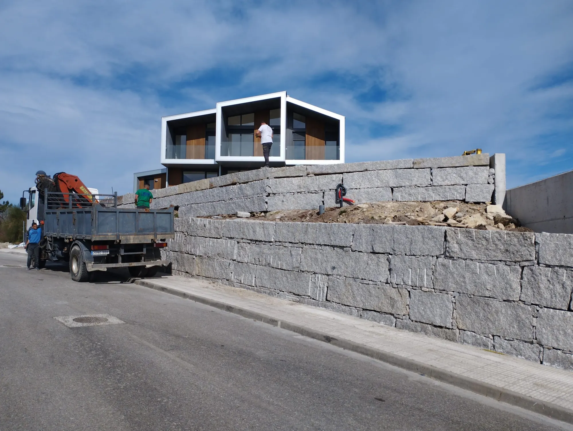 Muro de contención de sillería junto a un vial, con camión grúa en obra